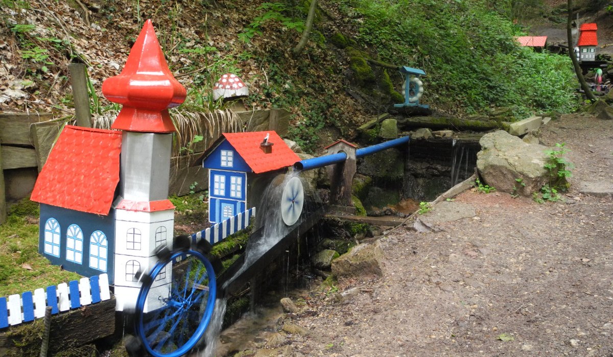 Miniatur-Wassermühle im Wald mit bunten Häuschen und Wasserrad. Ein kleiner Bach fließt durch die Anlage, umgeben von Bäumen und Laub., © Stadt Lorch