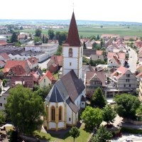 Luftaufnahme von Holzgerlingen mit einer Kirche im Vordergrund, umgeben von Häusern und grüner Landschaft im Hintergrund., © Natur.Nah. Schönbuch & Heckengäu