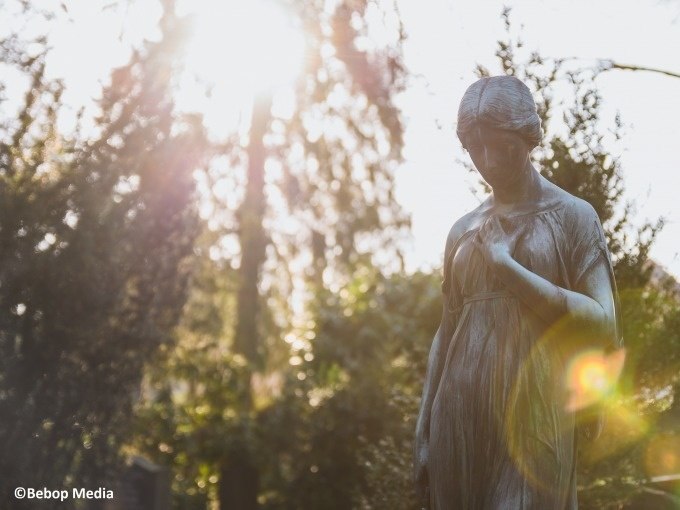 Eine melancholische Statue einer Frau auf einem Friedhof, beleuchtet von der untergehenden Sonne, die durch die Bäume scheint., © Eigenbetrieb Tourismus und Citymanagement Schorndorf