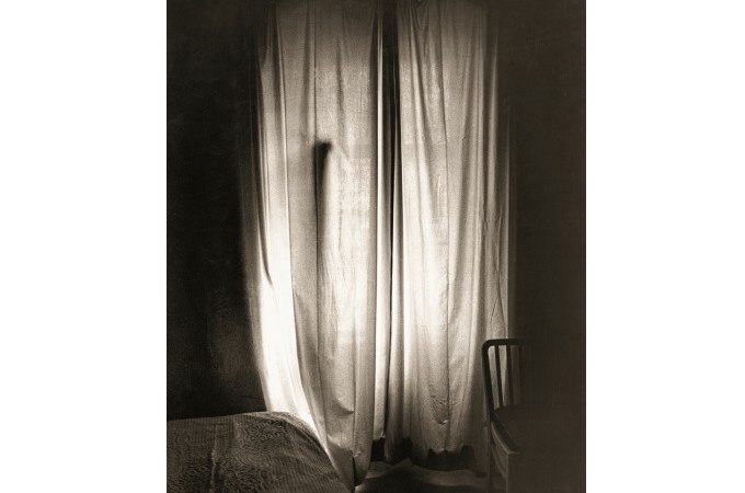 Ein schattiger Raum mit einem Bett und einem Stuhl. Licht fällt durch einen geschlossenen Vorhang und erzeugt eine ruhige Atmosphäre., © Kunsthalle Göppingen Ein schattiger Raum mit einem Bett und einem Stuhl. Licht fällt durch einen geschlossenen Vorhang und erzeugt eine ruhige Atmosphäre., © Kunsthalle Göppingen