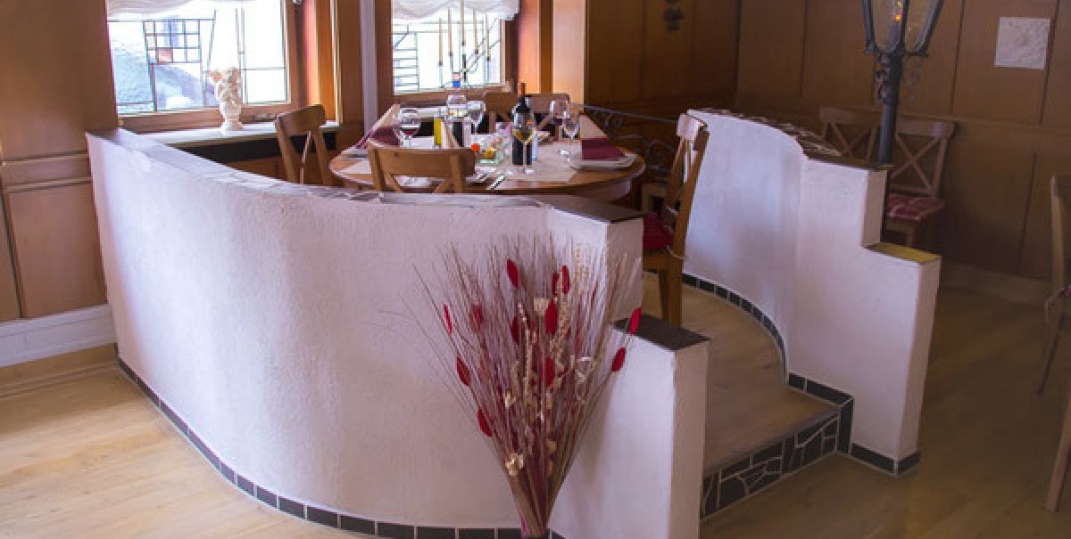 Ein runder Tisch in einem gemütlichen Restaurant, umgeben von Holzmöbeln und Dekoration. Ein Strauß mit roten Akzenten steht im Vordergrund.