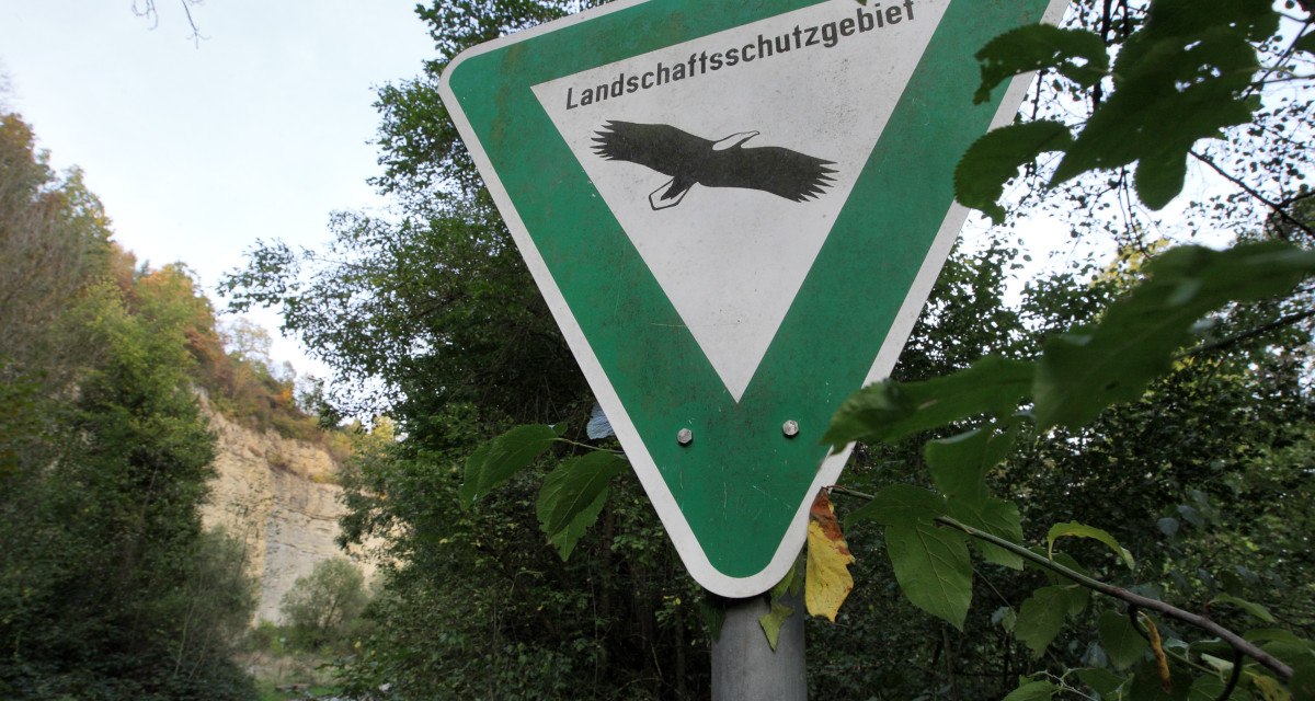 Schild 'Landschaftsschutzgebiet' mit Vogelmotiv, umgeben von Bäumen. Ein Weg führt durch die grüne Landschaft im Hintergrund., © Remstal Tourismus e.V.