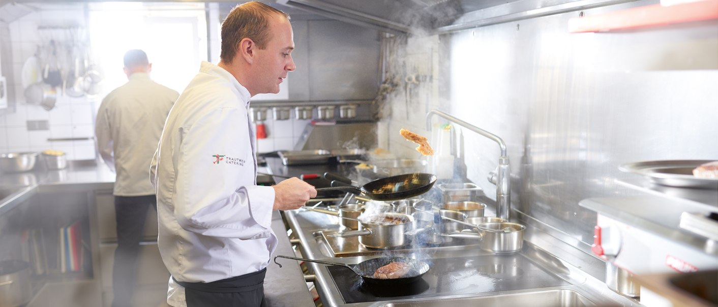 Ein Koch in weißer Uniform brät Fleisch in einer Pfanne in einer professionellen Küche. Im Hintergrund ist ein weiterer Koch zu sehen., © SMG, Jean-Claude Winkler Ein Koch in weißer Uniform brät Fleisch in einer Pfanne in einer professionellen Küche. Im Hintergrund ist ein weiterer Koch zu sehen., © SMG, Jean-Claude Winkler