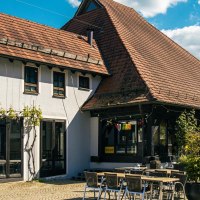 Traditionelles Gebäude mit Ziegeldach und Restaurant auf dem Kelterplatz in Metzingen. Sonnenschirme und Tische im Freien, umgeben von Pflanzen., © Stuttgart-Marketing GmbH, Sarah Schmid