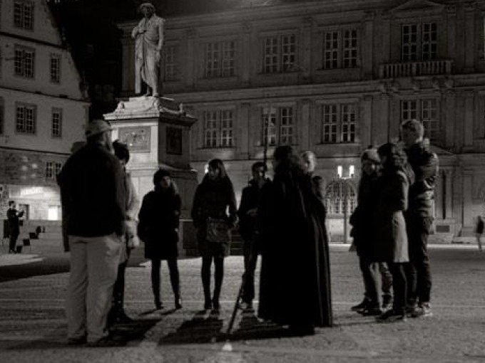 Eine Gruppe von Menschen steht nachts vor einer Statue auf einem Platz in Stuttgart. Die Szene wirkt geheimnisvoll und historisch., © Stuttgarter Geister