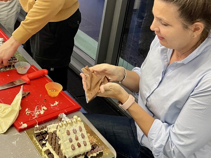 Eine Person dekoriert ein Lebkuchenhaus mit Schokolade und Süßigkeiten. Im Hintergrund sind weitere Dekorationsmaterialien zu sehen., © Alfred Ritter GmbH & Co. KG | Waldenbuch Eine Person dekoriert ein Lebkuchenhaus mit Schokolade und Süßigkeiten. Im Hintergrund sind weitere Dekorationsmaterialien zu sehen., © Alfred Ritter GmbH & Co. KG | Waldenbuch