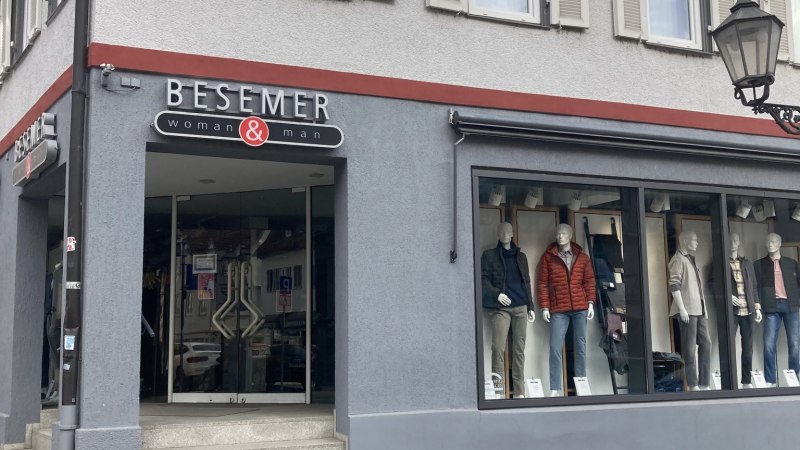 Modehaus Besemer in N&uuml;rtingen mit Schaufensterpuppen und Eingangst&uuml;r. Graue Fassade mit roten Akzenten, Kopfsteinpflaster davor., &copy; Lena Besemer