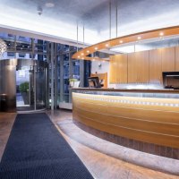 Moderne Hotelrezeption mit geschwungener Holztheke, beleuchtetem Empfangsbereich und Dreht&uuml;r im Hintergrund. Elegantes, einladendes Ambiente., &copy; Kronen Hotel GmbH