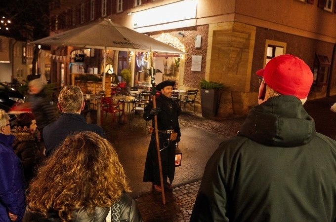 Ein Nachtwächter in historischer Kleidung führt eine Gruppe durch eine nächtliche, beleuchtete Straße., © Stadt Waldenbuch