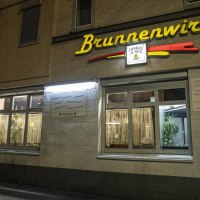 Das Restaurant Brunnenwirt bei Nacht, beleuchtet mit gelbem Schriftzug. Ein Mann steht an einem Tisch vor dem Eingang., &copy; SMG, Sarah Schmid