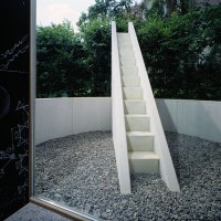 Weiße Treppe in rundem Kiesbereich, umgeben von Bäumen. Links Tafel mit Zeichnungen., © TOMAS