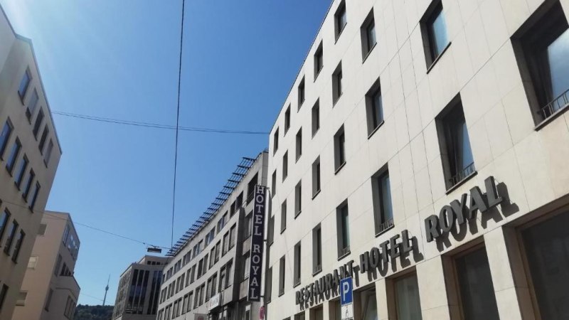 Ein modernes Gebäude mit dem Schriftzug 'Hotel Royal' unter blauem Himmel. Die Straße ist von weiteren Gebäuden gesäumt., © Hotel Royal Ein modernes Gebäude mit dem Schriftzug 'Hotel Royal' unter blauem Himmel. Die Straße ist von weiteren Gebäuden gesäumt., © Hotel Royal