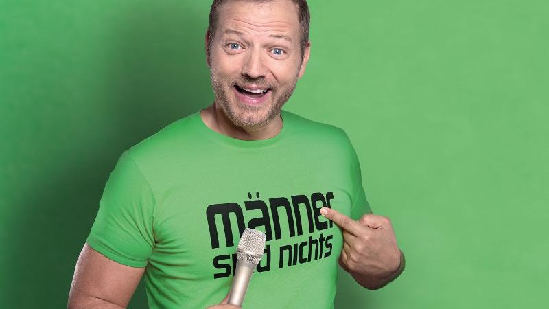 Ein Mann in einem gr&uuml;nen T-Shirt mit der Aufschrift 'M&auml;nner sind nichts' h&auml;lt ein Mikrofon und zeigt auf sein Shirt vor einem gr&uuml;nen Hintergrund., &copy; Ludwigsburg