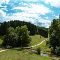 Vogelperspektive auf eine gr&uuml;ne Landschaft mit W&auml;ldern, Wiesen und einem kleinen Bach. Ein Weg schl&auml;ngelt sich durch die Szenerie unter einem blauen Himmel., &copy; Landkreis G&ouml;ppingen