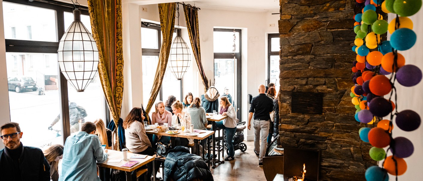Gemütliches Café mit großen Fenstern, Menschen an Tischen, bunte Kugeln an der Wand und ein Kamin. Warme, einladende Atmosphäre., © Stuttgart-Marketing GmbH, Sarah Schmid Gemütliches Café mit großen Fenstern, Menschen an Tischen, bunte Kugeln an der Wand und ein Kamin. Warme, einladende Atmosphäre., © Stuttgart-Marketing GmbH, Sarah Schmid