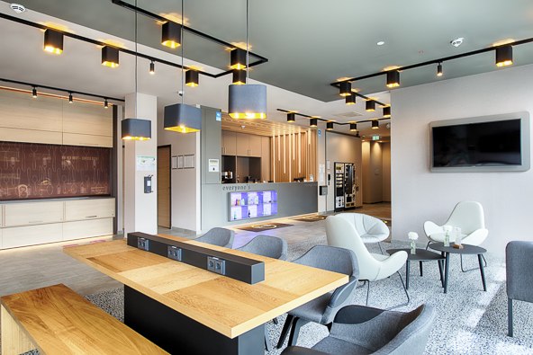 Moderne Lobby mit stilvollen Sitzgelegenheiten, Holztisch, Deckenbeleuchtung und einem großen Bildschirm an der Wand., © B&B Hotel Stuttgart-Neckarhafen