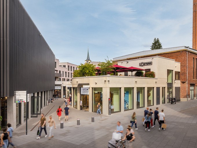 Einkaufsstra&szlig;e in der Outletcity Metzingen mit modernen Geb&auml;uden, Gesch&auml;ften und vielen Passanten bei sonnigem Wetter., &copy; Schlienz-Tours GmbH & Co.KG