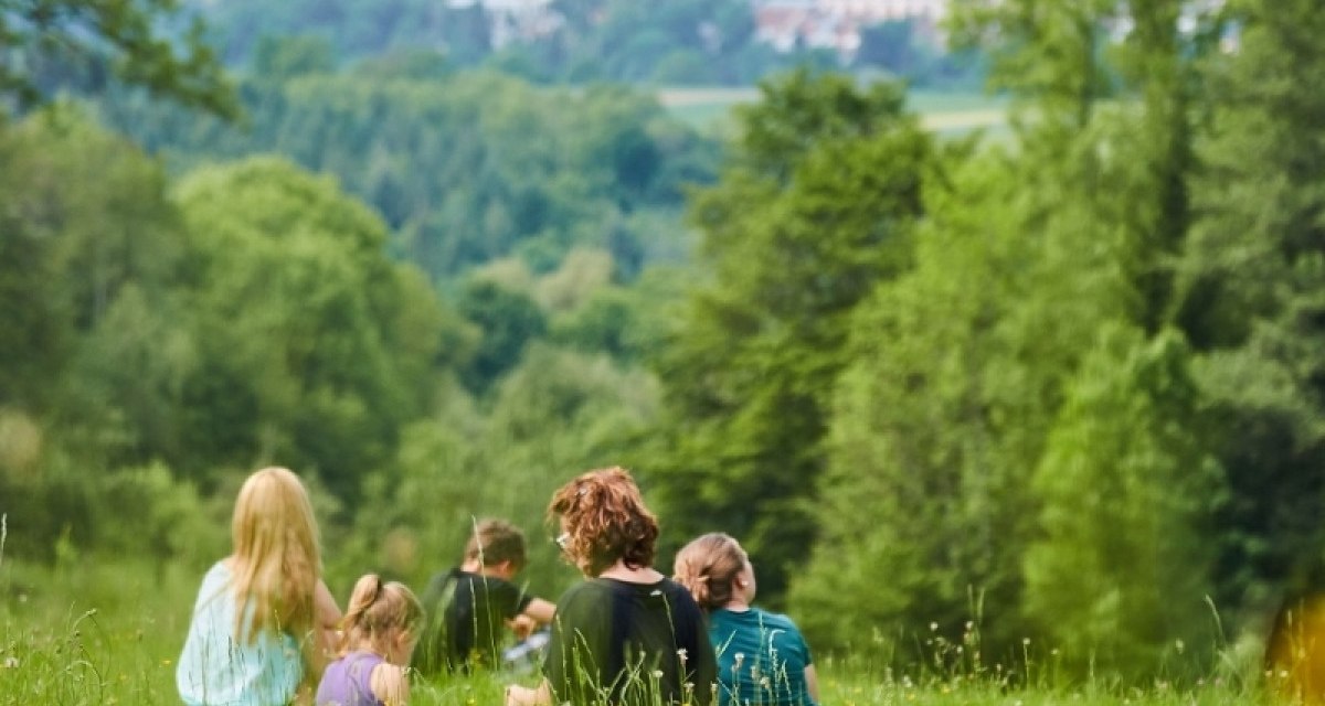 Gruppe von Menschen sitzt auf einer grünen Wiese, umgeben von Bäumen, mit Blick auf ein Dorf in der Ferne., © Natur.Nah. Schönbuch & Heckengäu Gruppe von Menschen sitzt auf einer grünen Wiese, umgeben von Bäumen, mit Blick auf ein Dorf in der Ferne., © Natur.Nah. Schönbuch & Heckengäu
