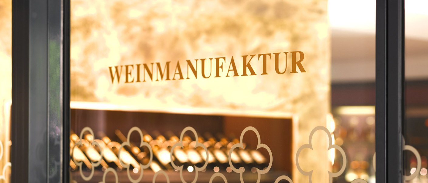 Der Eingang der Weinmanufaktur zeigt den Schriftzug auf einer Glastür. Im Hintergrund sind Weinflaschen zu sehen., © Weinmanufaktur Stuttgart Der Eingang der Weinmanufaktur zeigt den Schriftzug auf einer Glastür. Im Hintergrund sind Weinflaschen zu sehen., © Weinmanufaktur Stuttgart