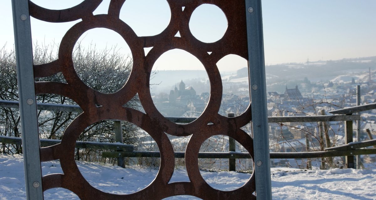 Metallskulptur mit Kreisen im Vordergrund, verschneite Landschaft und Stadt im Hintergrund. Winterliche Szene mit klarer Sicht., © Land der 1000 Hügel - Kraichgau-Stromberg Metallskulptur mit Kreisen im Vordergrund, verschneite Landschaft und Stadt im Hintergrund. Winterliche Szene mit klarer Sicht., © Land der 1000 Hügel - Kraichgau-Stromberg