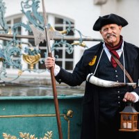 Mann in historischer Nachtwächterkleidung mit Hellebarde und Laterne vor einem verzierten Brunnen., © Stadt Nürtingen