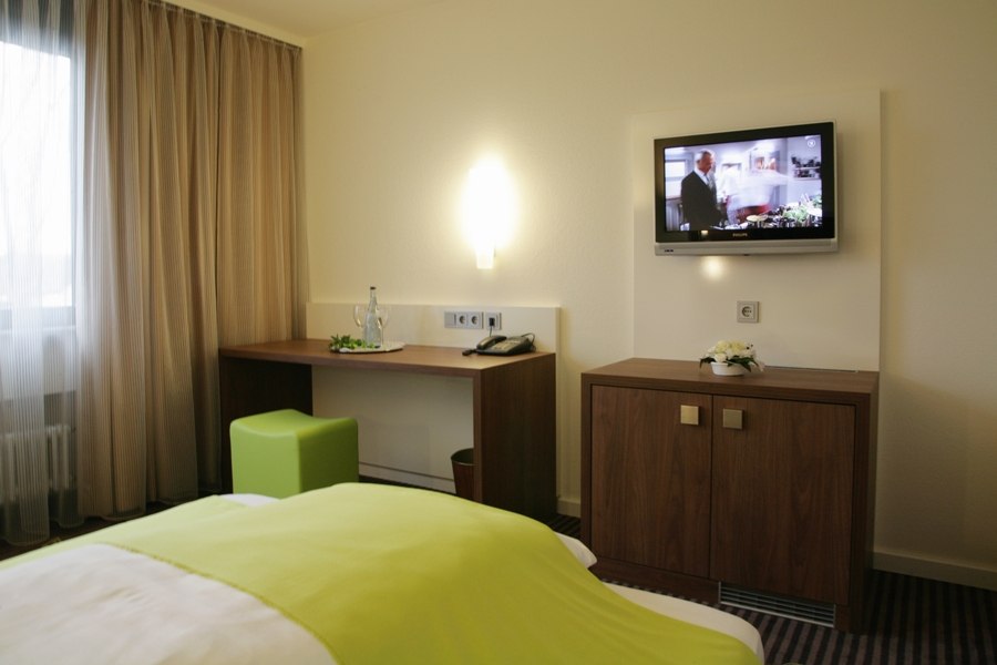 Ein modernes Einzelzimmer mit grünem Bettüberwurf, Schreibtisch, Fernseher an der Wand und einem Fenster mit Vorhängen., © Hotel Fuchsen Ein modernes Einzelzimmer mit grünem Bettüberwurf, Schreibtisch, Fernseher an der Wand und einem Fenster mit Vorhängen., © Hotel Fuchsen