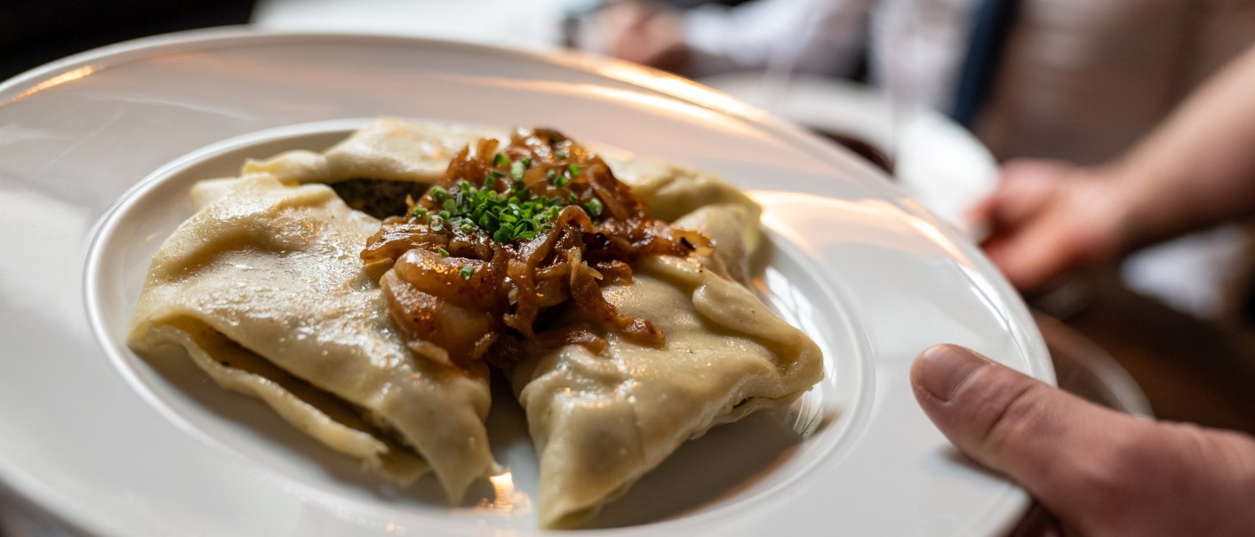 Ein Teller mit Maultaschen, garniert mit R&ouml;stzwiebeln und Schnittlauch, wird in einem Restaurant serviert., &copy; Stuttgart-Marketing GmbH, Martina Denker