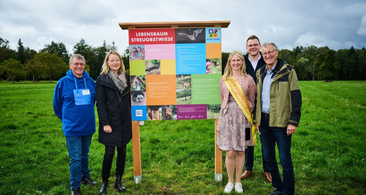 F&uuml;nf Personen posieren vor einem bunten Informationsschild mit der Aufschrift 'Lebensraum Streuobstwiese' auf einer gr&uuml;nen Wiese., &copy; Natur.Nah. Sch&ouml;nbuch & Heckeng&auml;u