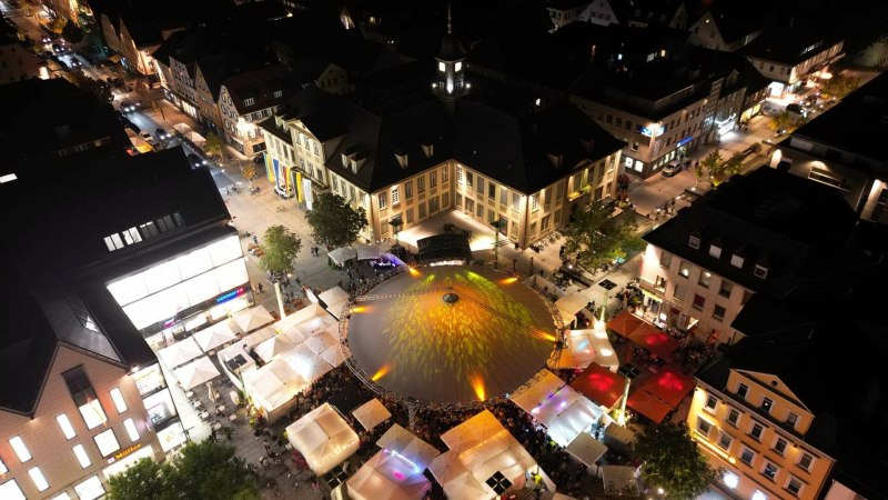 Luftaufnahme des G&ouml;ppinger Weinfests bei Nacht. Beleuchtete Zelte und Menschenmengen f&uuml;llen den Platz vor einem gro&szlig;en Geb&auml;ude.
