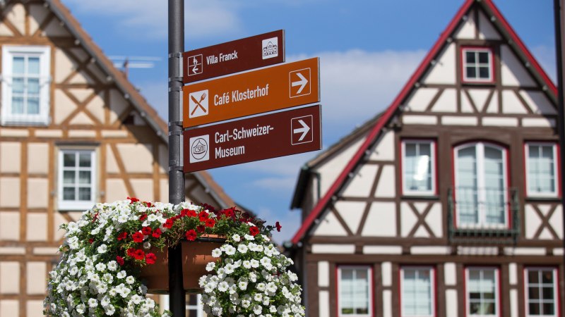 Ein Wegweiser mit Blumen vor Fachwerkhäusern auf dem Marktplatz von Murrhardt. Schilder zeigen zu Villa Franck, Café Klosterhof und Carl-Schweizer-Museum., © Stuttgart-Marketing GmbH, Achim Mende