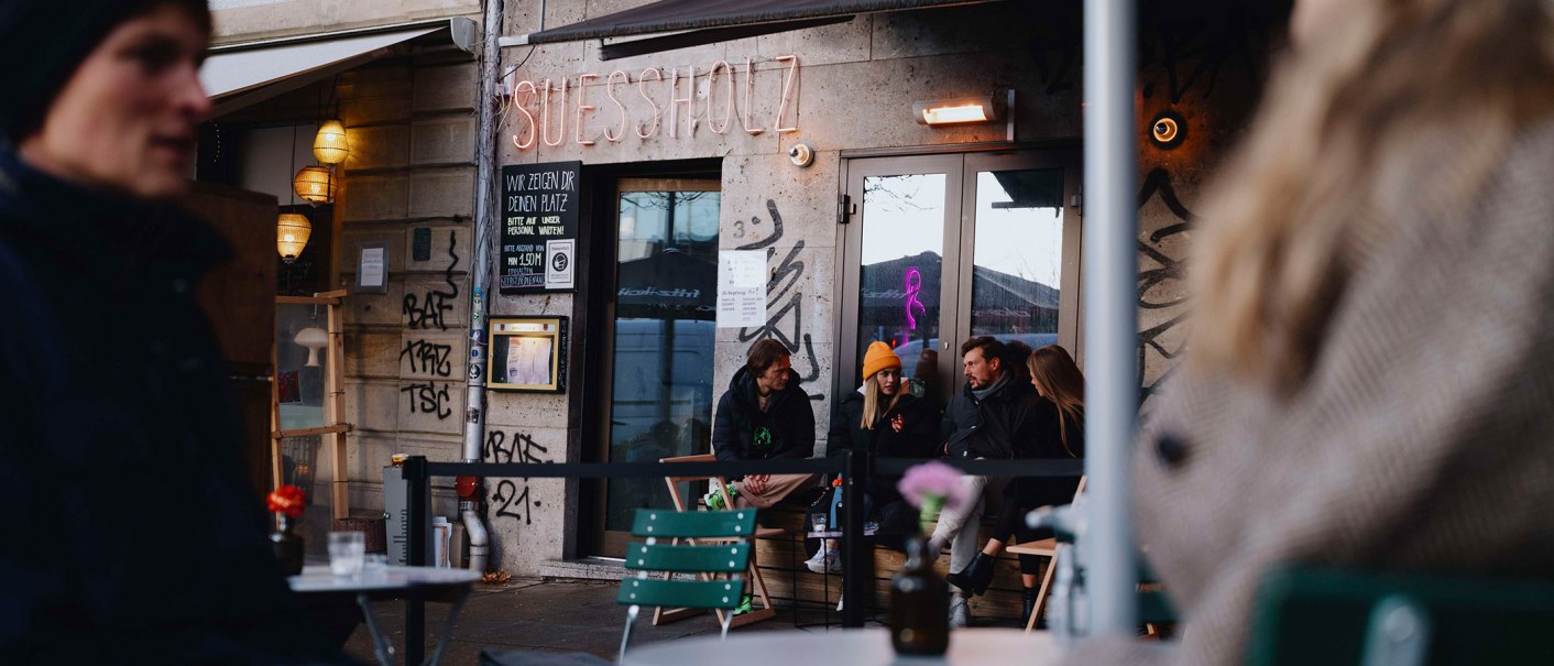 Außenansicht des Cafés 'Suessholz' im Leonhardsviertel. Menschen sitzen draußen, unterhalten sich. Graffiti an den Wänden, Neonlicht im Fenster., © Stuttgart-Marketing GmbH, Alwin Maigler