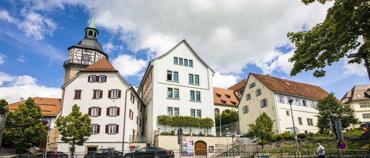Historische Geb&auml;ude in Backnang, darunter das Bandhaus und Helferhaus, vor einem blauen Himmel mit Wolken. B&auml;ume und Stra&szlig;enschilder im Vordergrund., &copy; SMG, Sarah Schmid