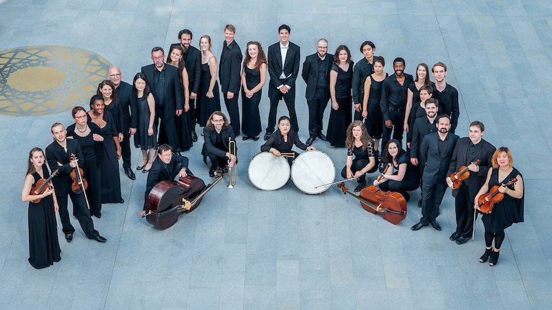 Ein Orchester in schwarzer Kleidung steht in einem Kreis auf einem grauen Boden mit goldenen Mustern., &copy; Kulturstiftung Hohenlohe