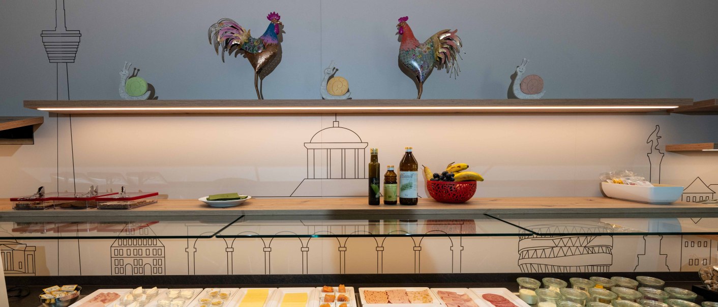 Ein reichhaltiges Fr&uuml;hst&uuml;cksbuffet mit K&auml;se, Aufschnitt, Gem&uuml;se und Joghurt vor einer Wand mit Stuttgart-Motiven und dekorativen H&auml;hnen., &copy; TOMAS