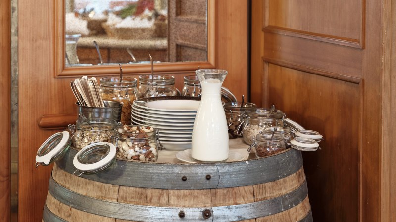 Ein Frühstücksbuffet auf einem Weinfass mit Milch, Nüssen, Besteck und Tellern in einem rustikalen Restaurant., © Badhotel Restaurant Stauferland