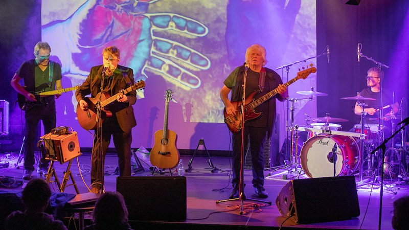 Eine Band performt auf einer B&uuml;hne mit Gitarren, Bass und Schlagzeug. Im Hintergrund sind bunte Projektionen von H&auml;nden zu sehen., &copy; Interessengemeinschaft Kultur Sindelfingen / B&ouml;blingen e.V.