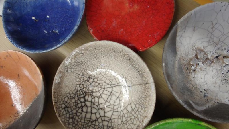 Bunte Raku-Keramikschalen in Blau, Rot, Weiß, Orange und Grün mit charakteristischen Rissen auf einem Tisch angeordnet., © Kunstschule Labyrinth