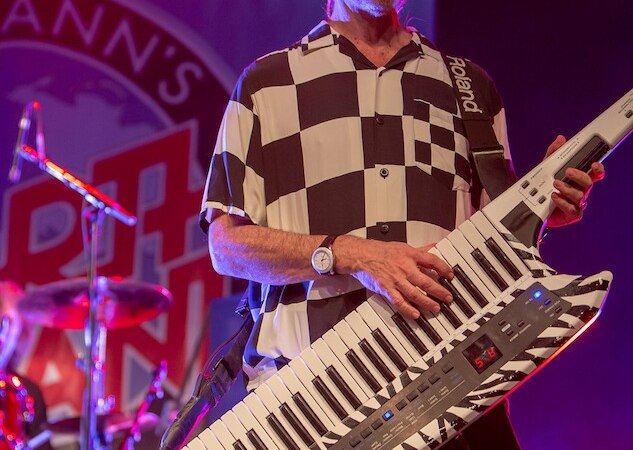 Ein Musiker mit Hut spielt eine Keytar auf der Bühne. Im Hintergrund ist ein Banner von Manfred Mann's Earth Band zu sehen., © die Halle Kulturinitiative e.V.