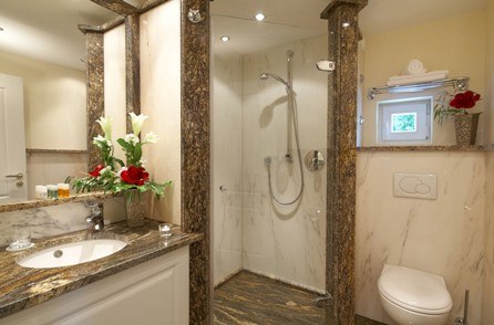 Elegantes Badezimmer mit Marmorverkleidung, Dusche, Waschbecken und WC. Dekoriert mit roten Blumen und Handtüchern., © Jeanette Bender Elegantes Badezimmer mit Marmorverkleidung, Dusche, Waschbecken und WC. Dekoriert mit roten Blumen und Handtüchern., © Jeanette Bender