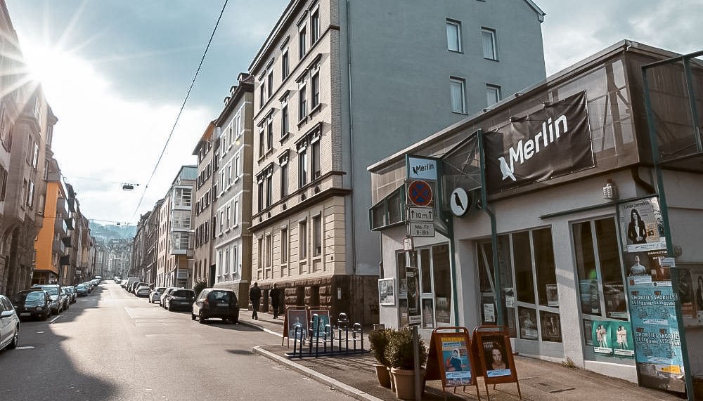 Straßenszene in Stuttgart mit dem Kulturzentrum Merlin e.V. rechts im Bild. Die Sonne scheint, Autos parken entlang der Straße., © Merlin, Stuttgart Straßenszene in Stuttgart mit dem Kulturzentrum Merlin e.V. rechts im Bild. Die Sonne scheint, Autos parken entlang der Straße., © Merlin, Stuttgart