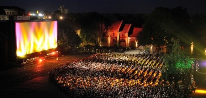 Ein n&auml;chtliches Open-Air-Kino mit vielen Zuschauern vor einer gro&szlig;en, beleuchteten Leinwand. Die Umgebung ist von B&auml;umen und Geb&auml;uden umgeben., &copy; KinoKult e.V.