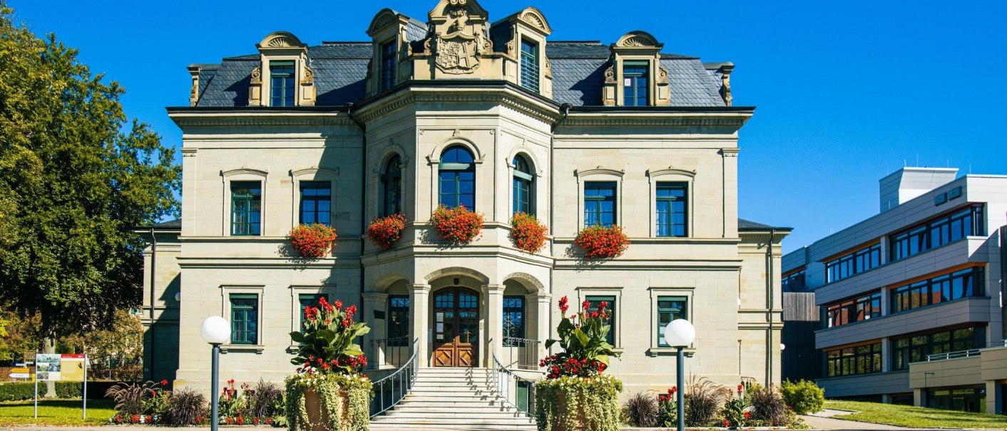 Das Neue Schloss in Gaildorf mit blumengeschmückten Fenstern und moderner Architektur im Hintergrund. Ein sonniger Tag mit klarem Himmel., © Stuttgart-Marketing GmbH, Sarah Schmid