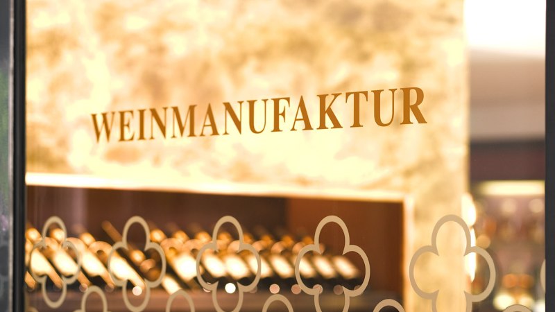 Der Eingang der Weinmanufaktur zeigt den Schriftzug auf einer Glast&uuml;r. Im Hintergrund sind Weinflaschen zu sehen., &copy; Weinmanufaktur Stuttgart