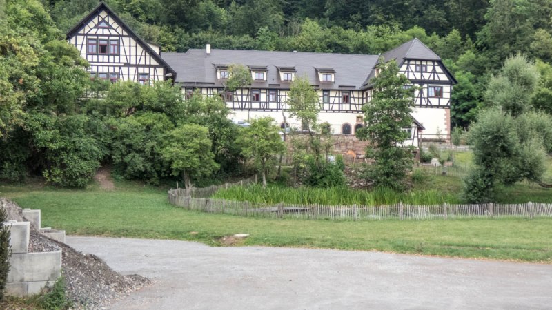 Ein gro&szlig;es Fachwerkhaus steht inmitten von B&auml;umen und gr&uuml;ner Landschaft. Ein Weg f&uuml;hrt an einer Wiese vorbei zum Haus., &copy; Natur.Nah. Sch&ouml;nbuch & Heckeng&auml;u