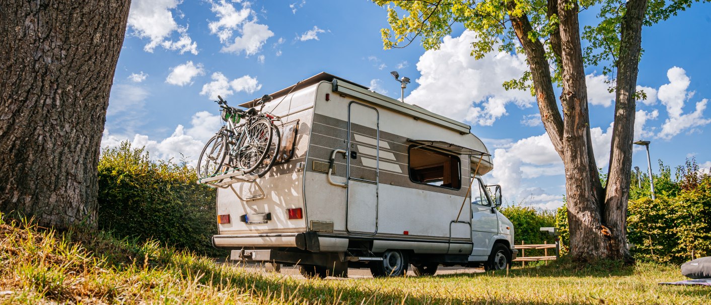 Ein Wohnmobil mit Fahrrädern am Heck steht auf einem grünen Stellplatz unter Bäumen. Der Himmel ist blau mit weißen Wolken., © Stuttgart-Marketing GmbH, Thomas Niedermüller