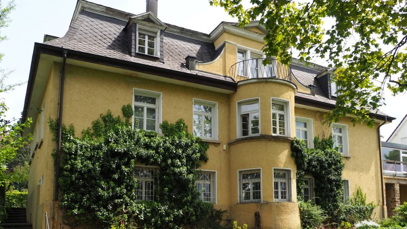 Eine gelbe Villa mit Efeu bewachsen, umgeben von einem gepflegten Garten. Die Architektur ist klassisch mit mehreren Fenstern und einem kleinen Balkon., &copy; Ruoff Stiftung