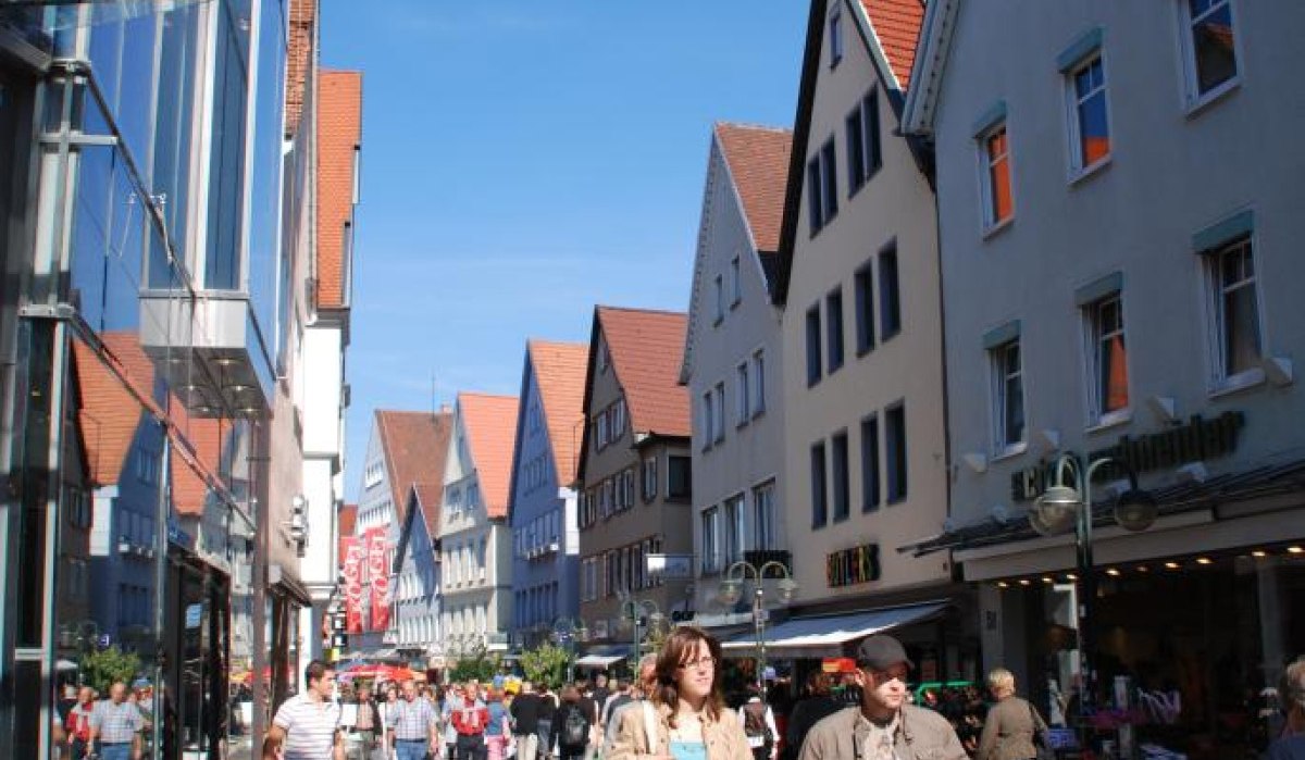Belebte Einkaufsstraße in Reutlingen mit historischen Giebelhäusern und modernen Glasfassaden. Menschen flanieren bei sonnigem Wetter., © Mythos Schwäbische Alb im Landkreis Reutlingen e.V. Belebte Einkaufsstraße in Reutlingen mit historischen Giebelhäusern und modernen Glasfassaden. Menschen flanieren bei sonnigem Wetter., © Mythos Schwäbische Alb im Landkreis Reutlingen e.V.