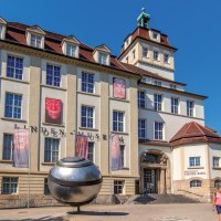 Das Linden-Museum in Stuttgart bei sonnigem Wetter. Vor dem Gebäude sind Plakate und eine große silberne Kugel zu sehen. Menschen spazieren vorbei., © Stuttgart-Marketing GmbH, Achim Mende Das Linden-Museum in Stuttgart bei sonnigem Wetter. Vor dem Gebäude sind Plakate und eine große silberne Kugel zu sehen. Menschen spazieren vorbei., © Stuttgart-Marketing GmbH, Achim Mende