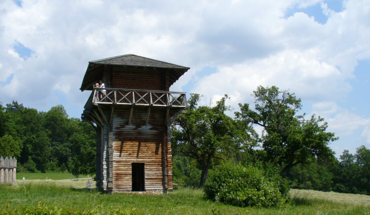Ein hölzerner römischer Wachturm auf einer Wiese, umgeben von Bäumen und einem bewölkten Himmel. Ein hölzerner römischer Wachturm auf einer Wiese, umgeben von Bäumen und einem bewölkten Himmel.