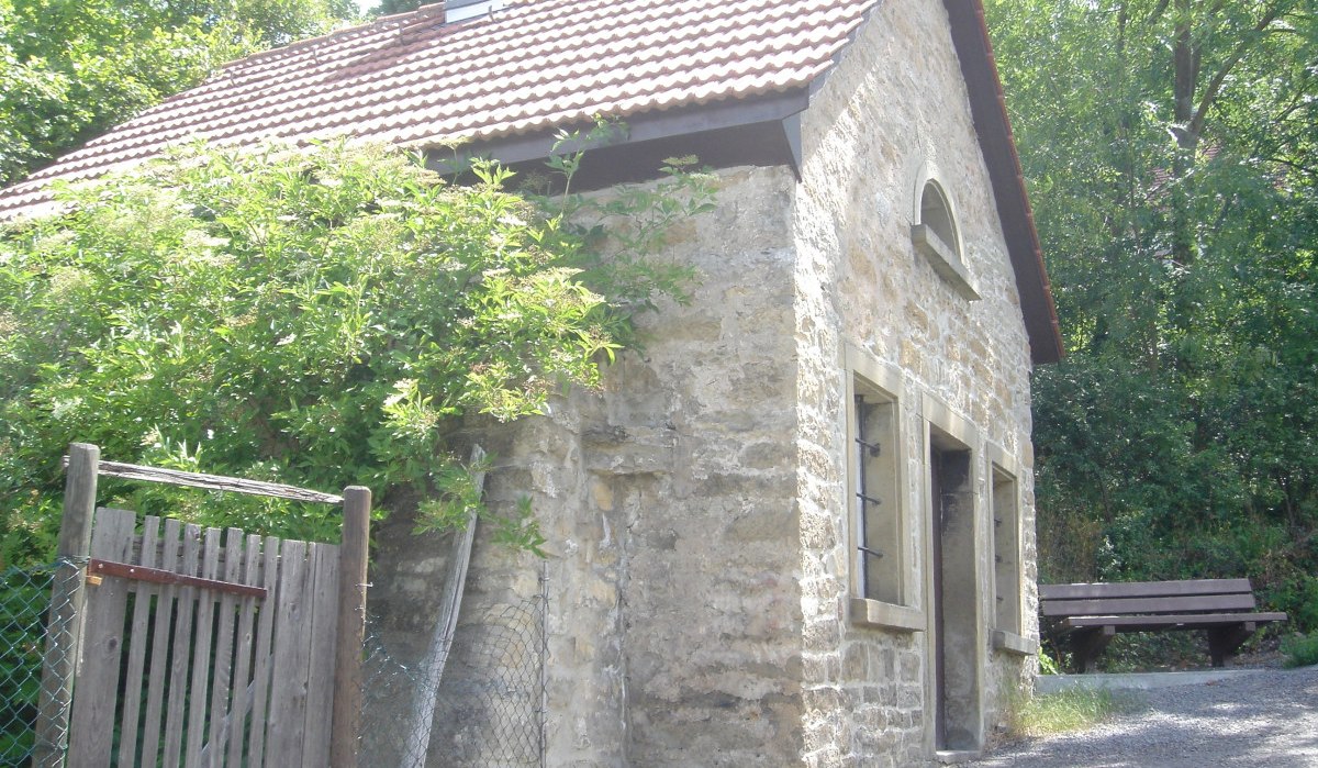 Kleines Steinhaus mit Ziegeldach, umgeben von Bäumen. Ein Holzzaun und eine Bank sind sichtbar. Es wirkt ländlich und ruhig., © Land der 1000 Hügel - Kraichgau-Stromberg